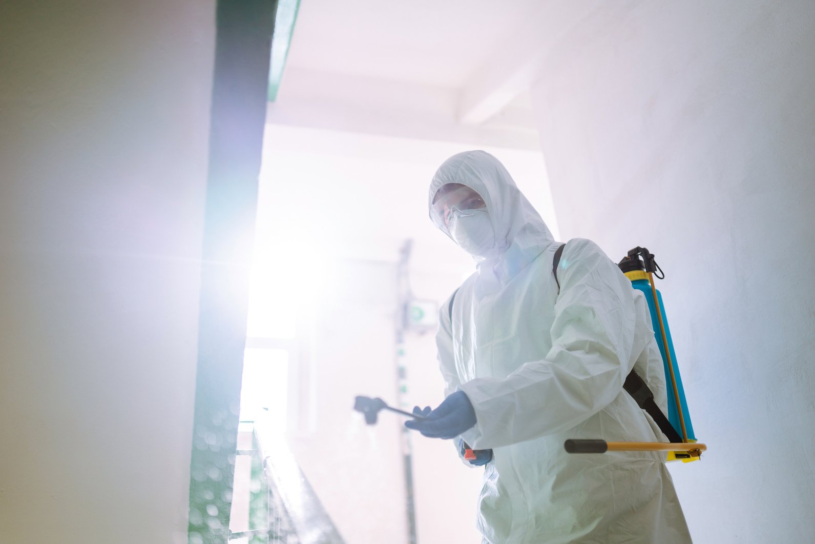 Man in Hazmat suit, protective gloves and goggles use sprayer equipment disinfect the entrance.